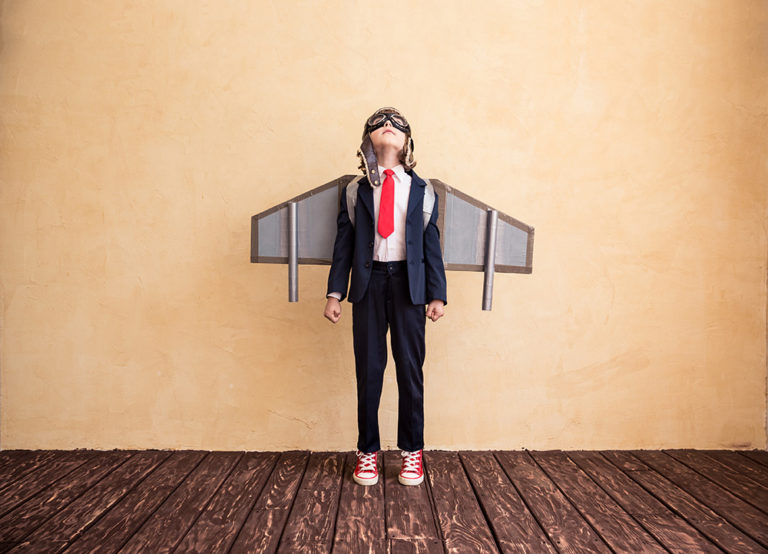Young boy with cardboard wings strapped to his back.